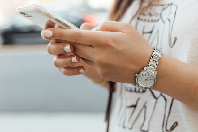 woman with white nails scrolling on phone while outside